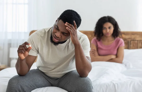 Triste homem negro segurando pílula sexual, namorada irritada assistindo ele — Fotografia de Stock