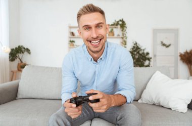 Kanepede oturup video oyunu oynayan heyecanlı adam.