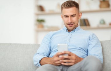 Evde akıllı telefon kullanan yakışıklı bir yetişkin.