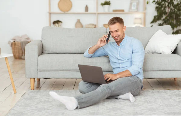 Szabadúszó férfi ül a padlón telefonnal és PC-vel — Stock Fotó