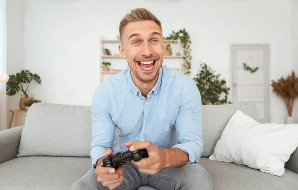 Junger Kerl sitzt auf Sofa und spielt Videospiele — Stockfoto