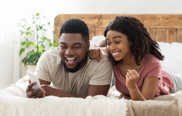 Feliz casal negro comemorando o sucesso, segurando smartphone — Fotografia de Stock