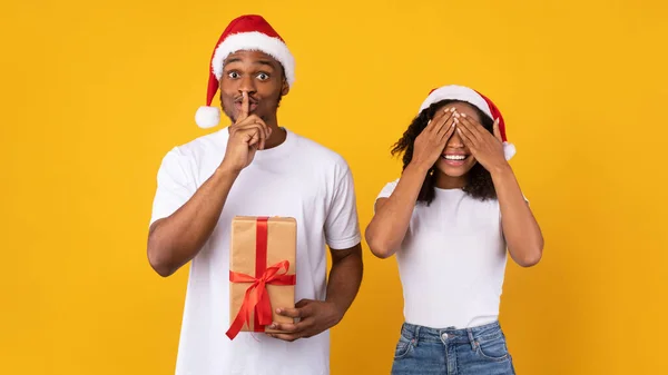 Novio sosteniendo regalo de Navidad Gesturing Hush Novia felicitante, fondo amarillo — Foto de Stock