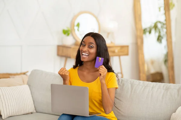 Shopping online. Donna afroamericana con computer portatile e carta di credito che fa gesto SI sopra grande sconto a casa — Foto Stock