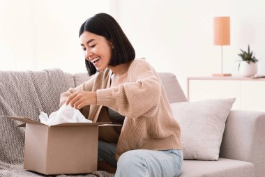 İnternetten alışveriş yaptıktan sonra paketleri açan mutlu Asyalı kadın.