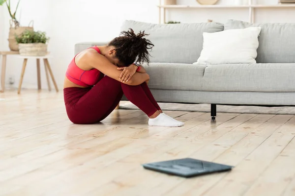 アフリカ系アメリカ人女性が自宅で体重計の近くに座って泣いている — ストック写真