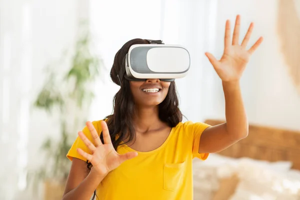 Futuristic stay home hobby. African American woman in virtual reality headset playing interactive computer game indoors