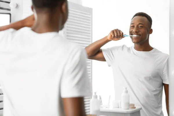 Hombre negro cepillando dientes con cepillo de dientes de pie en el baño en interiores — Foto de Stock