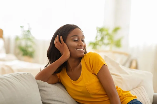 Χαλαρωτικό πρωινό Σαββατοκύριακου στο σπίτι. Χαρούμενη μαύρη γυναίκα που αναπαύεται στον αναπαυτικό καναπέ. — Φωτογραφία Αρχείου