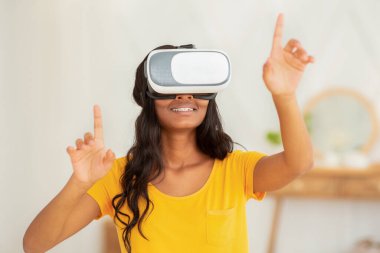 Modern ev hobileri. Sanal gerçeklik kulaklığı takmış, kapalı alanda siber uzayı keşfeden Afro-Amerikan kadın.