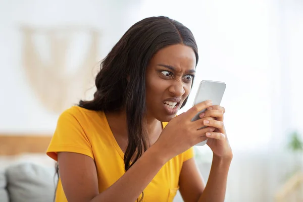 Mujer afroamericana recibiendo malas noticias, enojada con su teléfono inteligente en casa —  Fotos de Stock