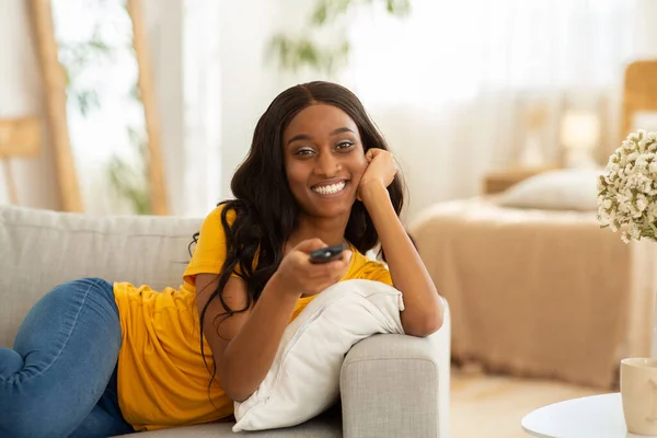 Aktivitas liburan akhir pekan. Milenial perempuan kulit hitam dengan remote control switching channel di TV di rumah, salinan ruang — Stok Foto