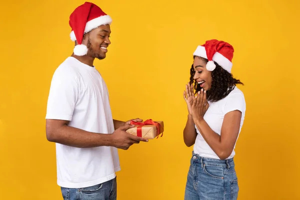 검은 남자 친구가 노란 배경에 여자 친구에게 크리스마스 선물을 주는 모습 — 스톡 사진