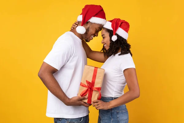 Чорна пара тримає різдвяний подарунок стоячи на жовтому тлі — стокове фото
