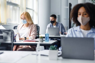 Karantinadan sonra çok ırklı işçilerle modern çalışma ofisi. Yöneticilerin masasında mavi antiseptik bulunan şişeye odaklan.