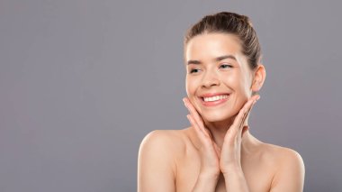 Gri stüdyo arka planında gülümseyen şehvetli genç kadın.