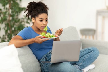 Afrikalı kadın salata yiyor. Akşam yemeği yiyor. Evde film izliyor.