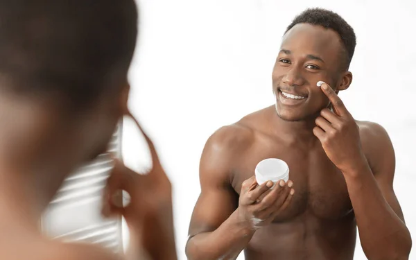 浴室に立って顔に保湿クリームを適用するアフリカ人男性 — ストック写真
