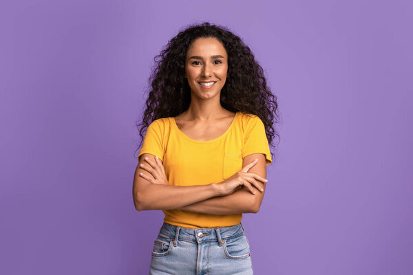Портрет уверенной молодой женщины, позирующей со сложенными руками на фиолетовом фоне
