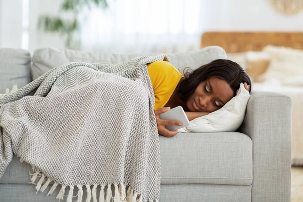 Καταθλιπτική Αφρο-Αμερικανίδα κυρία ξαπλωμένη στον καναπέ με smartphone και διαβάζοντας ανατρεπτικό μήνυμα, σε εσωτερικούς χώρους — Φωτογραφία Αρχείου