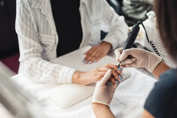 Dia de beleza e tratamentos de unhas. Mestre de manicure profissional em luvas de borracha faz procedimento remove verniz com um dispositivo de manicure elétrica para cliente afro-americano — Fotografia de Stock