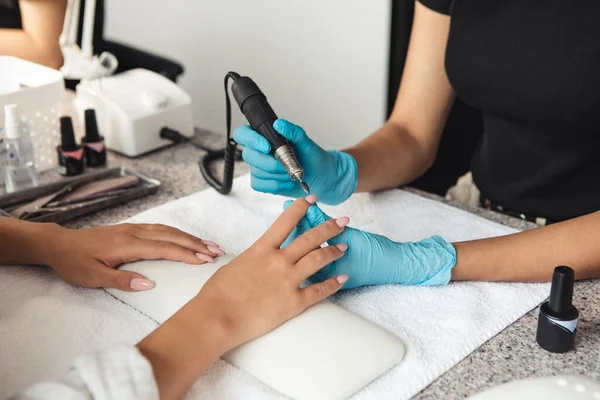 Moderne manicure in salon, hygiëne en sociale afstand. Afro-Amerikaanse vrouw met rubberen handschoenen vijlen nagels met elektrisch gereedschap aan tafel met apparatuur — Stockfoto