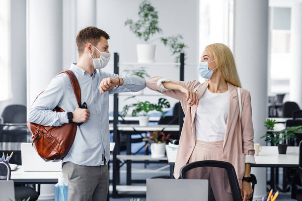 Современное приветствие с коллегой во время вспышки коронавируса. Тысячелетний парень и женщина в защитных масках пришли на работу утром и коснулись локтями, чтобы поздороваться.