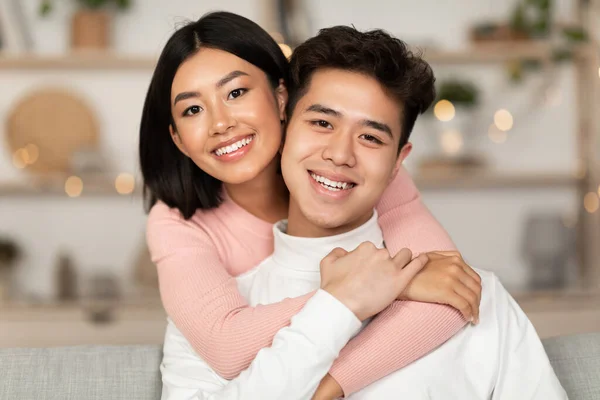 Azji para przytulanie uśmiech pozowanie siedzi na kanapie w domu — Zdjęcie stockowe