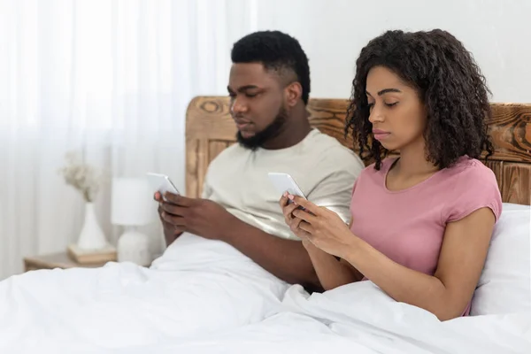 Pasangan Afrika-Amerika duduk di tempat tidur dan menggunakan smartphone mereka — Stok Foto