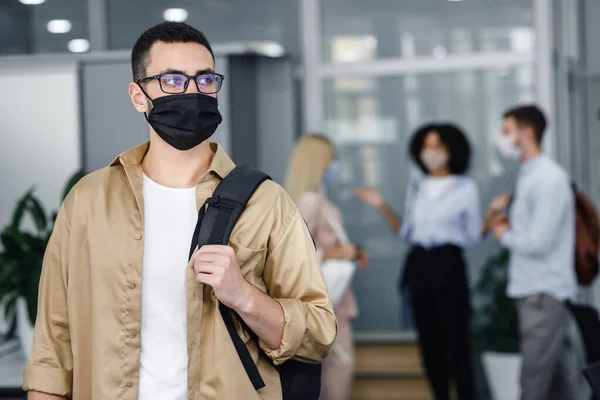 Pandemic and office work with people concept. Focus on millennial man in protective mask and glasses with backpack looking to the side