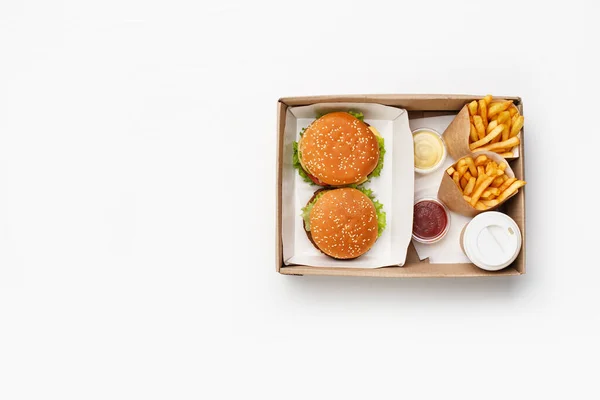Nowoczesny szybki lunch dla dwojga. Hamburger i cheeseburger, ketchup i sos w pojemnikach, frytki w papierowych torbach i filiżanka kawy w pudełku — Zdjęcie stockowe