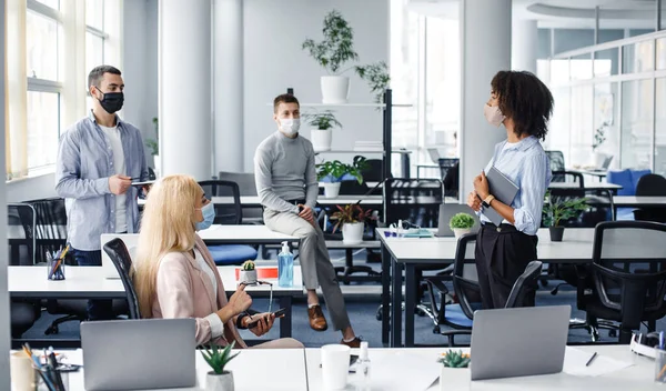 Informe sobre el trabajo, la reunión o la creación de equipos durante el brote de covidio-19. Joven mujer afroamericana con tableta habla a sus colegas en el interior de la oficina moderna — Foto de Stock