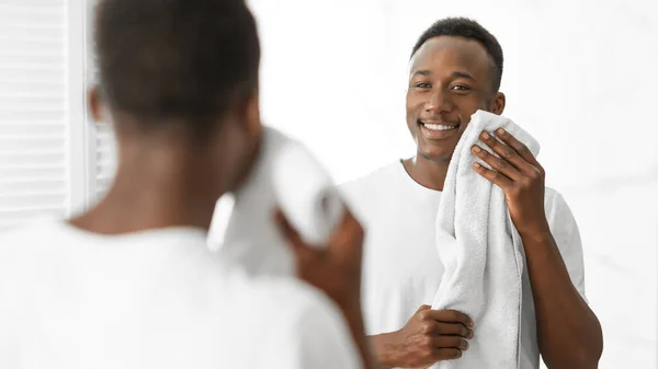 アフリカの男はバスルームに立って柔らかいタオルで顔を拭く — ストック写真