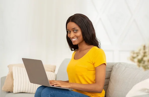 Donna d'affari nera positiva che utilizza il computer portatile per lavoro a distanza, istruzione o comunicazione a casa — Foto Stock