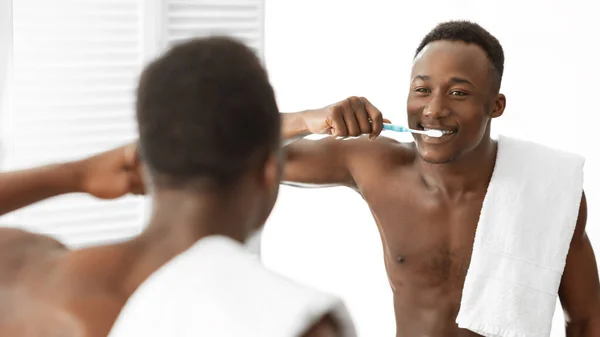 Negro hombre limpieza dientes con cepillo de pie en baño en interior — Foto de Stock