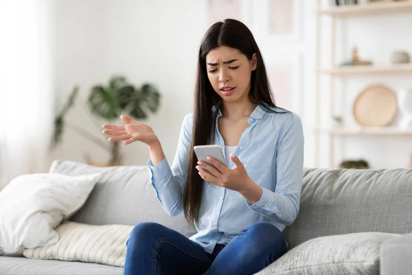 Slechte boodschap. geïrriteerde aziatische vrouw klagen over iets met mobiele telefoon in handen — Stockfoto