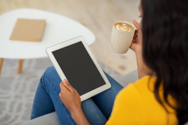 Kahveli genç siyah kadın evde boş ekranlı tablet bilgisayar kullanıyor, web sitenizin tasarımı için model.