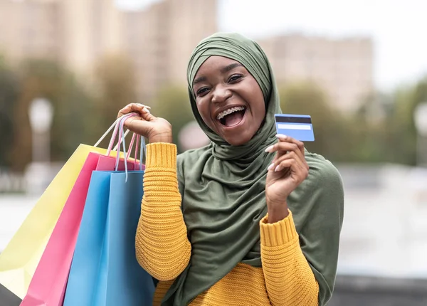 Nakit ikramiye. Dışarıda kredi kartı ve alışveriş torbaları tutan mutlu İslamcı kadın. — Stok fotoğraf