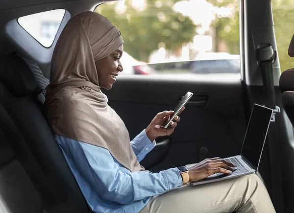 Afrikaanse moslim zakenvrouw met behulp van smartphone en werken op laptop in de auto — Stockfoto