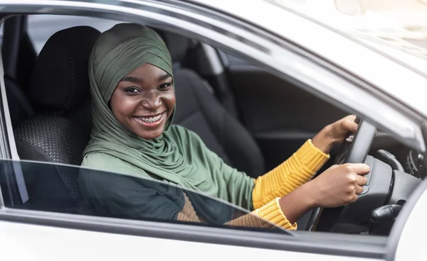 Jonge Afrikaanse moslim dame bestuurder zit op de voorbank in moderne auto — Stockfoto