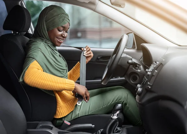 La seguridad primero. sonriente negro musulmán mujer en hiyab sujeción cinturón de seguridad en coche — Foto de Stock