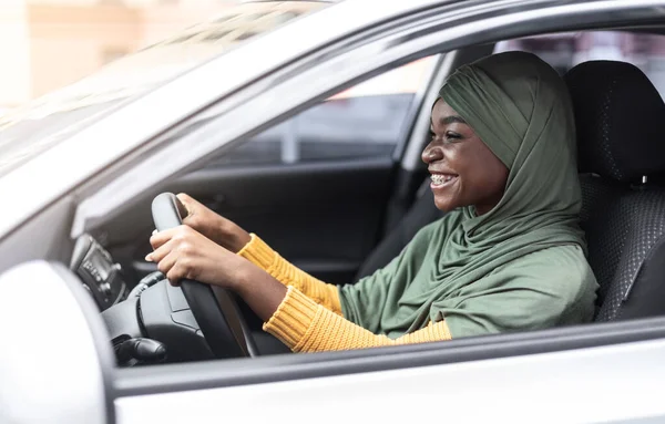 Conductora musulmana. Sonriente mujer negra islámica en hijab conduciendo su coche — Foto de Stock