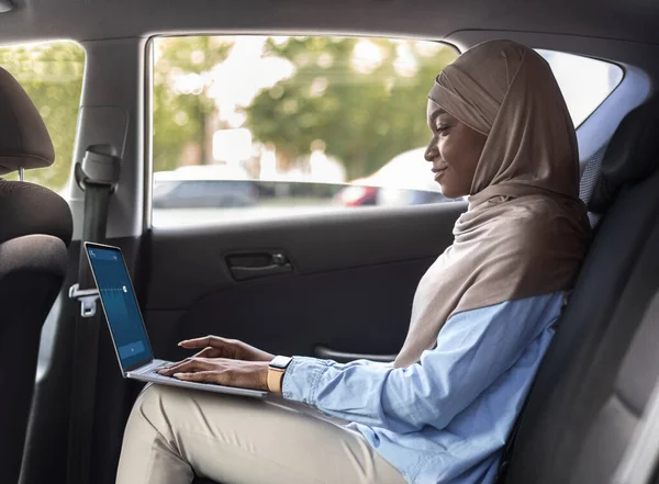 Zwarte moslim zakenvrouw met behulp van laptop in de auto terwijl gaan werken — Stockfoto