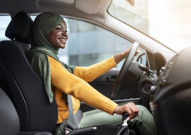 Kendine güvenen sürücü. Türbanlı gülümseyen Afrikalı Müslüman Kadın Modern Araba Sürüyor