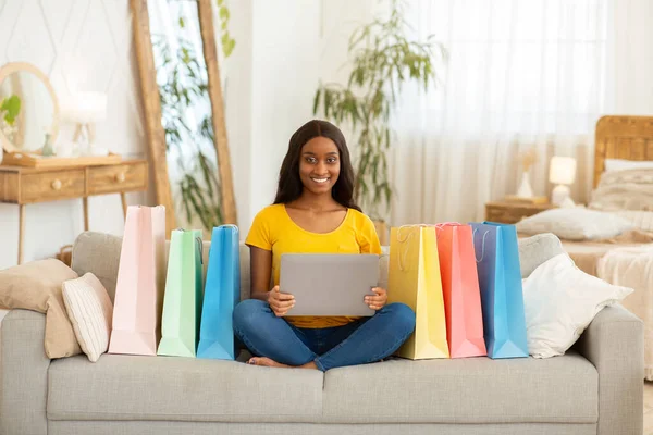 Millennial black woman with shopping bags using laptop computer for purchasing products online, indoors