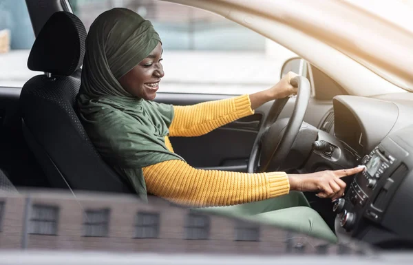 Auto afspeellijst. Vreugdevolle zwarte moslim vrouw rijden auto en muziek luisteren — Stockfoto