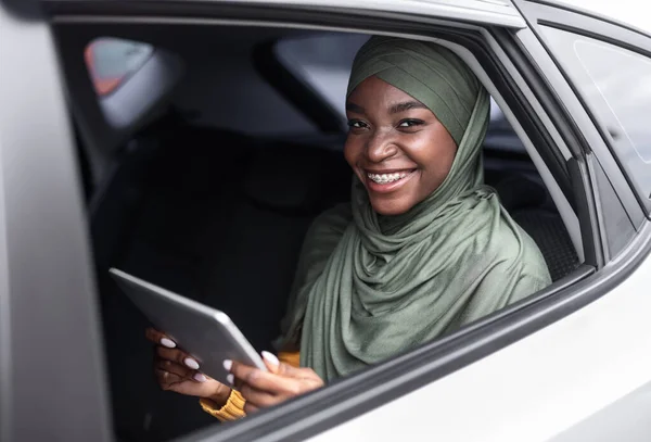 자동차 뒷자리에 앉아 디지털 태블릿을 들고 있는 행복 한 아프리카 이슬람 여성 — 스톡 사진