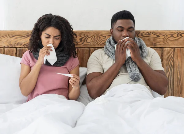 Pasangan afrika sakit duduk di tempat tidur, mengukur demam, bersin hidung — Stok Foto