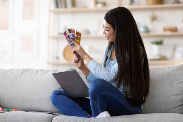 Курсы онлайн дизайна. Азиатская женщина держит цветные образцы и с помощью ноутбука дома — стоковое фото