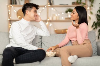 Asyalı çift, evde kalıp, koltukta oturarak eğleniyor.